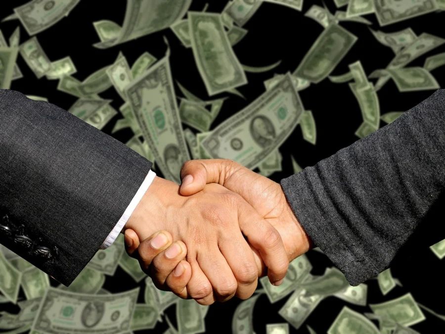 handshake over a laptop with crypto trading on screen